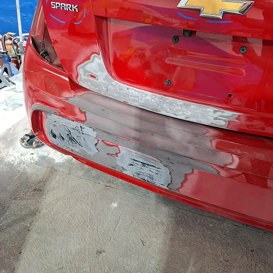 Chevrolet Spark rojo con el bumper trasero golpeado en el taller